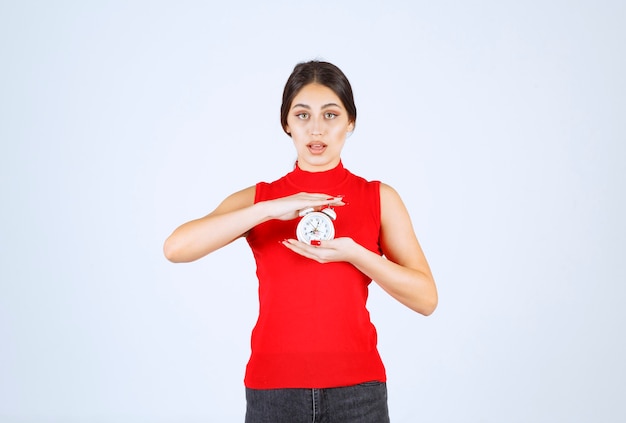 Menina de camisa vermelha segurando e promovendo um despertador.