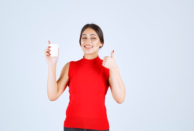 Foto grátis menina de camisa vermelha, tomando café e dando sinais positivos.