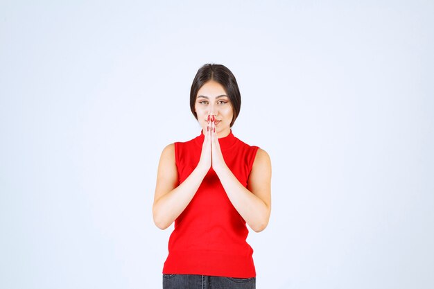 Foto grátis menina de camisa vermelha, unindo as mãos e orando.