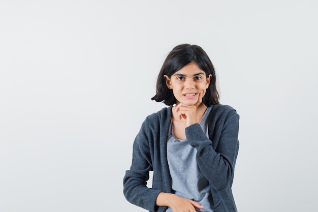 Menina de camiseta, jaqueta apoiando o queixo na mão e parecendo sensata