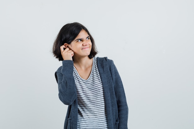 Menina de camiseta, jaqueta coçando a orelha e parecendo arrependida,