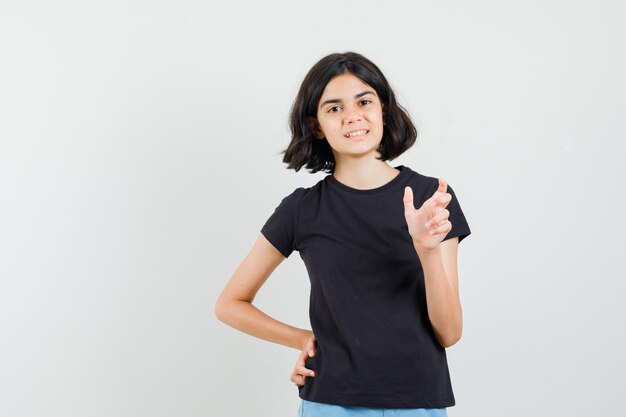 Menina de camiseta preta, shorts mostrando sinal de tamanho pequeno e olhando positiva, vista frontal.