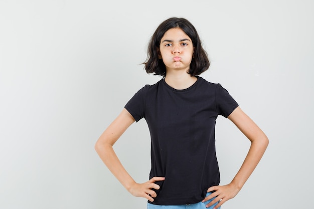 Menina de camiseta preta, shorts soprando nas bochechas e olhando furiosa, vista frontal.