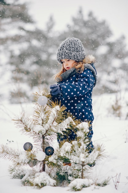 Menina de chapéu azul jogando em uma floresta de inverno