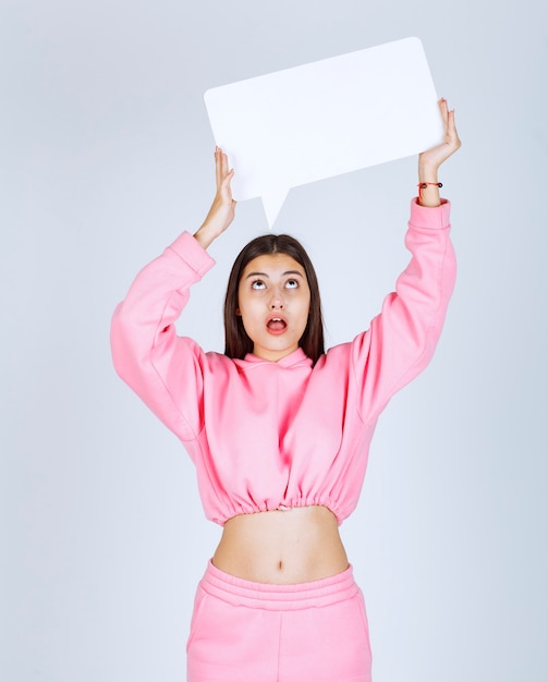 Foto grátis menina de pijama rosa segurando um quadro de idéias retangular em branco sobre a cabeça e pensando.