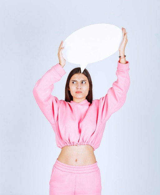 Foto grátis menina de pijama rosa, segurando uma prancha redonda de pensar e não gosta.