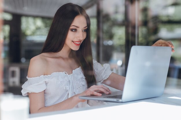 Menina de sorriso com lábios vermelhos pintados digitando em um laptop