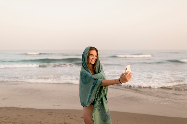 Menina de sorriso que está perto do litoral que toma o autorretrato do telefone móvel