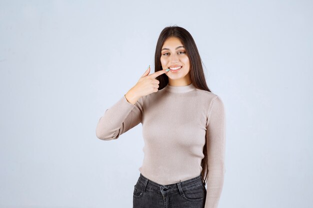 Menina de suéter cinza apontando o sorriso dela.