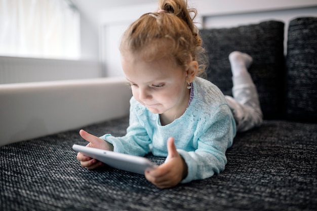 Foto grátis menina deitada no sofá e jogar jogo de tablet