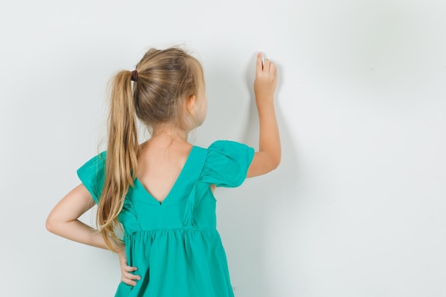 Menina desenho na parede com o dedo na vista traseira do vestido verde.