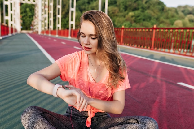 Menina desportiva sonhadora, olhando para o relógio após o treino. tiro ao ar livre de mulher refinada relaxante antes da maratona no estádio.