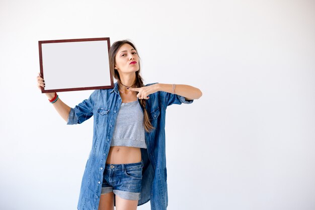 Menina determinada aponte o dedo para cartaz ou cartaz em branco branco