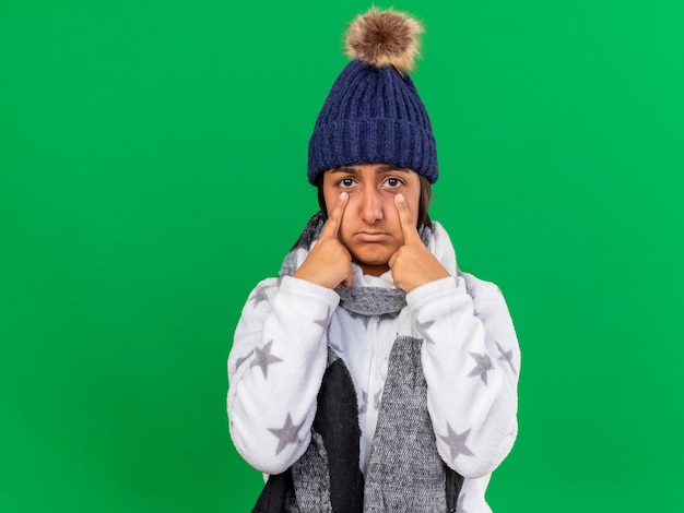 Foto grátis menina doente e triste com chapéu de inverno e lenço colocando os dedos nos olhos isolados sobre fundo verde