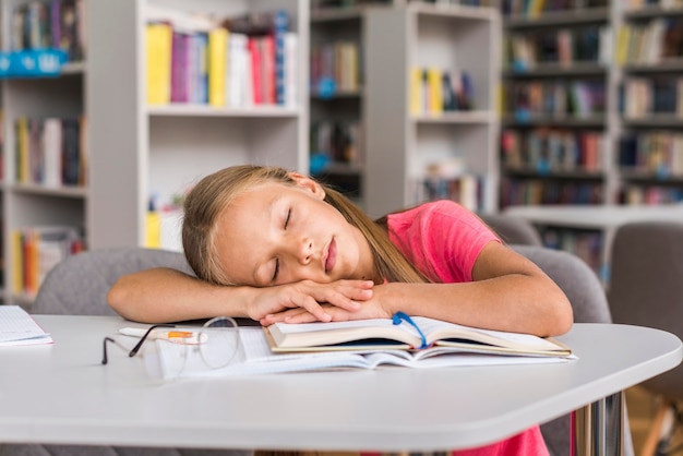 Menina dormindo em sua lição de casa na biblioteca