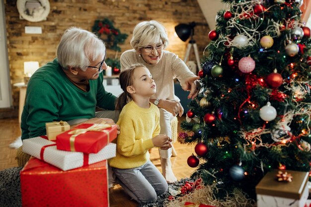 Menina e seus avós decorando a árvore de Natal juntos em casa