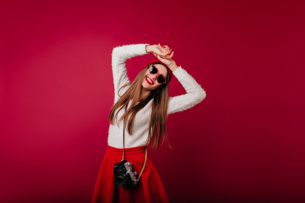 Menina elegante com chapéu e óculos de sol relaxando durante a sessão de fotos do estúdio