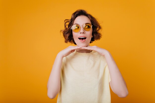 Menina elegante em uma camiseta da moda posando emocionalmente perto da parede amarela