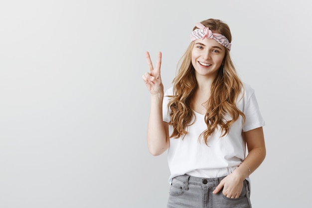 Menina elegante hipster em óculos de sol sorrindo feliz, mostrando o símbolo da paz