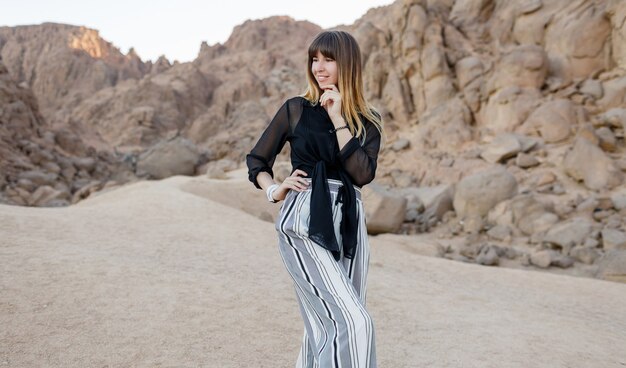 Menina elegante muito sorridente posando nas dunas de areia do deserto egípcio.