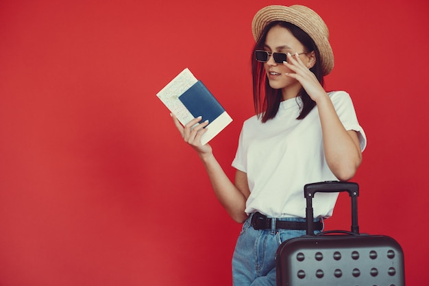 Menina elegante posando com equipamento de viagem em uma parede vermelha