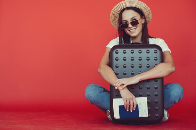 Menina elegante posando com equipamento de viagem em uma parede vermelha