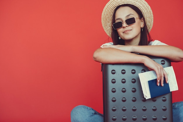 Menina elegante posando com equipamento de viagem em uma parede vermelha