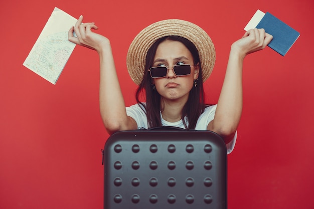 Menina elegante posando com equipamento de viagem em uma parede vermelha