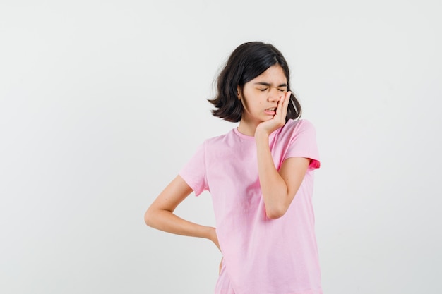 Menina em pé na pose de pensamento em t-shirt rosa e olhando esquecido, vista frontal.