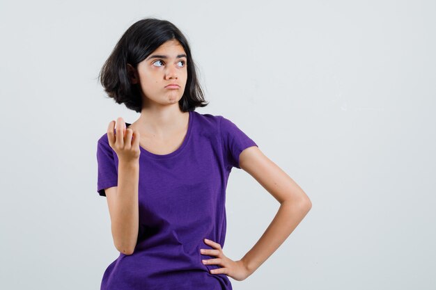 Menina em pé pensando em pose de camiseta e parecendo confusa