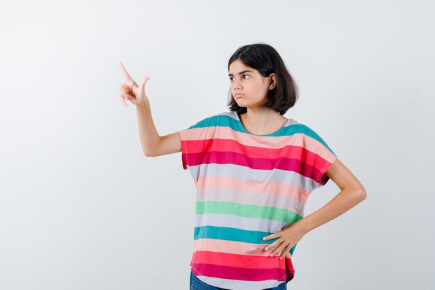 Menina em t-shirt apontando para cima e olhando focada, vista frontal.