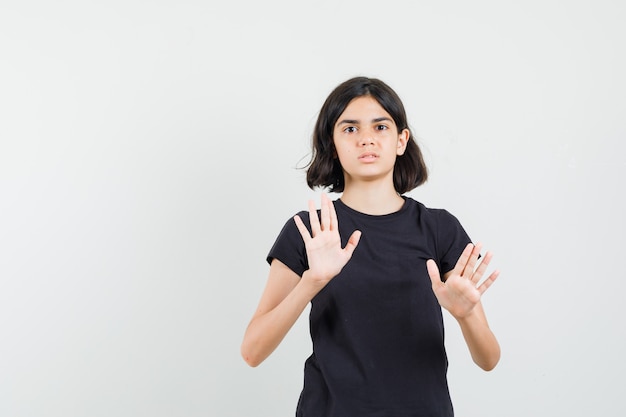 Menina em t-shirt preta mostrando gesto de recusa e parecendo irritada, vista frontal.