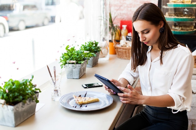 Menina em um café lê algo no tablet