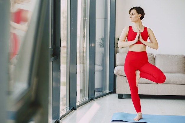 Menina em um uniforme vermelho esportes praticando ioga em casa