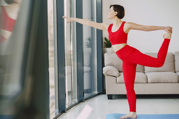 Menina em um uniforme vermelho esportes praticando ioga em casa