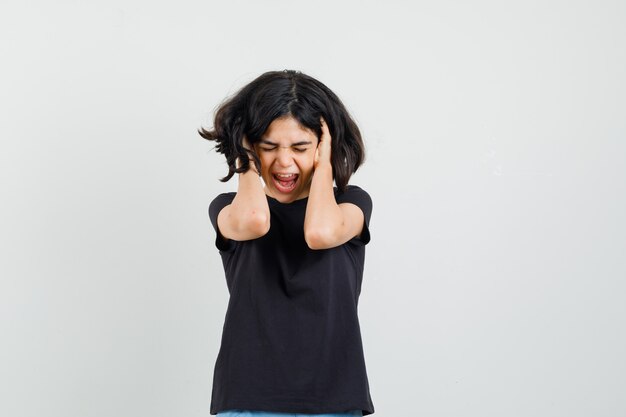 Menina em uma camiseta preta de mãos dadas no cabelo e parecendo irritada, vista frontal.