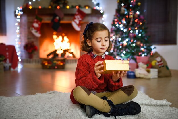 Menina em uma sala decorada para o Natal com caixa de presente dourada