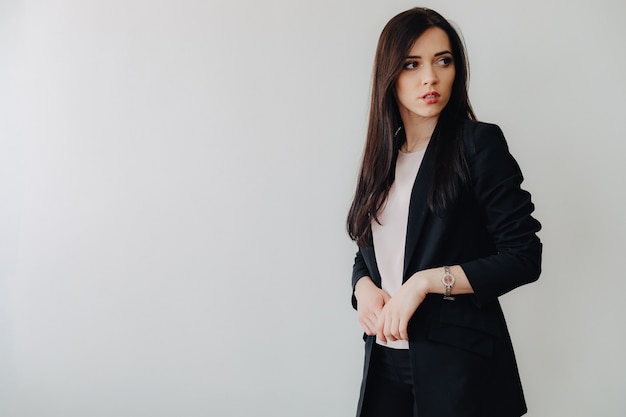 Menina emocional atrativa nova na roupa do estilo de negócio em um fundo branco liso em um escritório ou em uma audiência