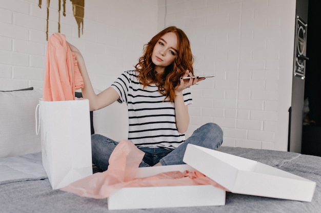 Foto grátis menina encantadora com telefone sentado na cama. jocund modelo feminino em jeans relaxantes no fim de semana.