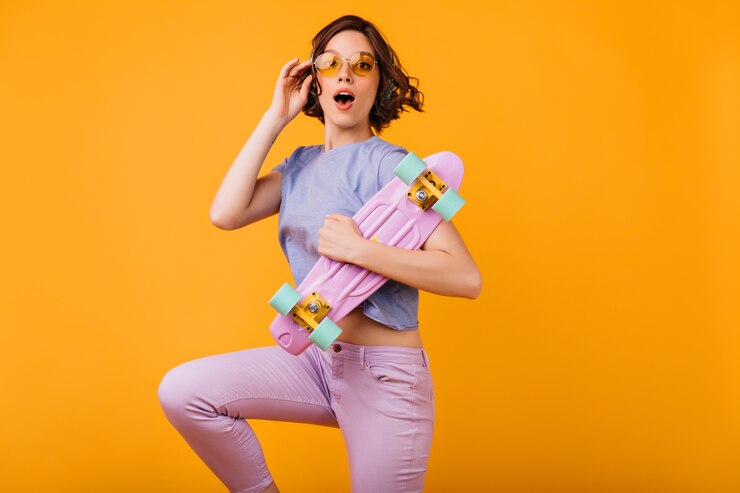 Foto grátis menina encantadora de óculos amarelos, posando com expressão de surpresa. foto interna de uma modelo feminina espetacular com skate rosa.