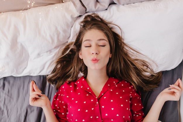 Menina encantadora medita na cama. foto aérea de senhora morena bonita relaxando com os olhos fechados.