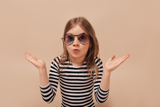 Menina engraçada e fofa de 6 anos posando para a câmera sobre um fundo bege com surpresas verdadeiras emoções