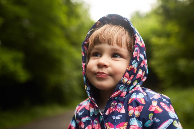 Menina engraçada no casaco de chuva fica no parque verde
