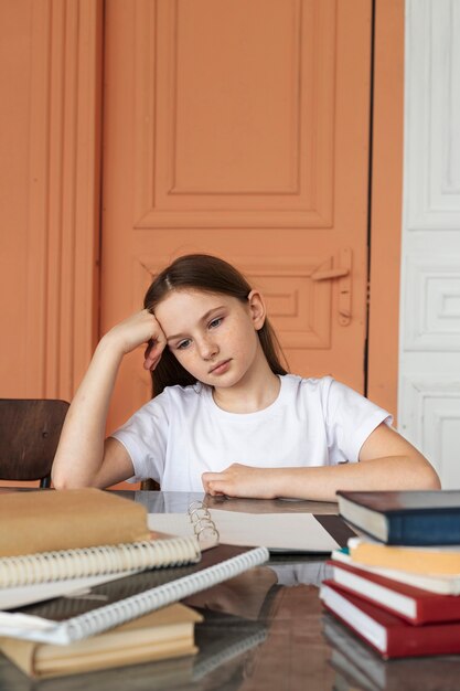 Menina entediada de tiro médio sentada na mesa com livros