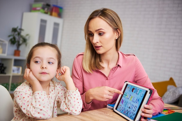 Menina entediada e a mãe estudando com o laptop em casa