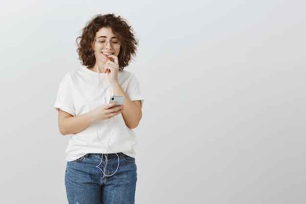 Menina enviando mensagens de texto arriscadas, animada com smartphone e usando fones de ouvido