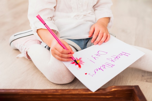 Menina escrevendo feliz dia das mães no papel