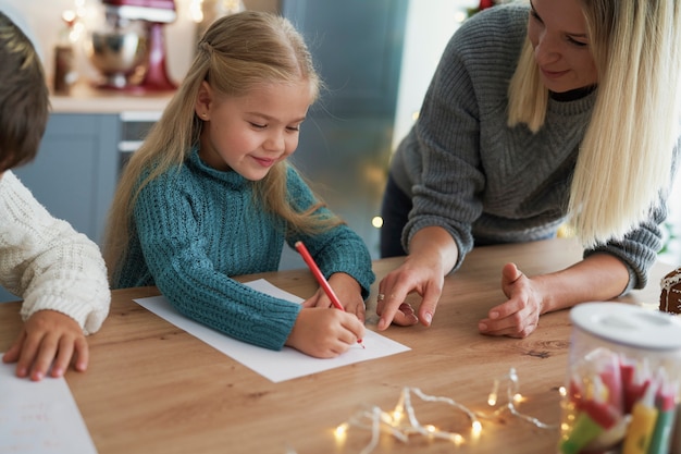 Menina escrevendo uma carta para o papai noel com a mãe