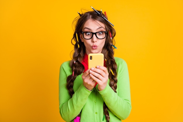 Menina espantada com o corte de cabelo a lápis lendo informações no smartphone isoladas sobre fundo de cor amarela