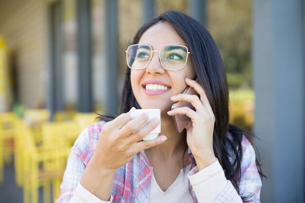 Menina esperta positiva do estudante que aprecia a conversa agradável do telefone